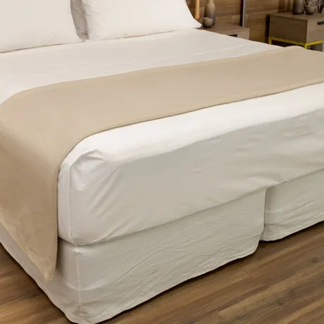 Frazada beige extendida a los pies de una cama de hotel
