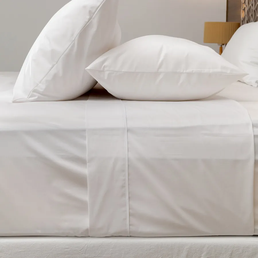 Embozo de sábana blanca sobre la cama, con dos almohadas apoyadas detrás